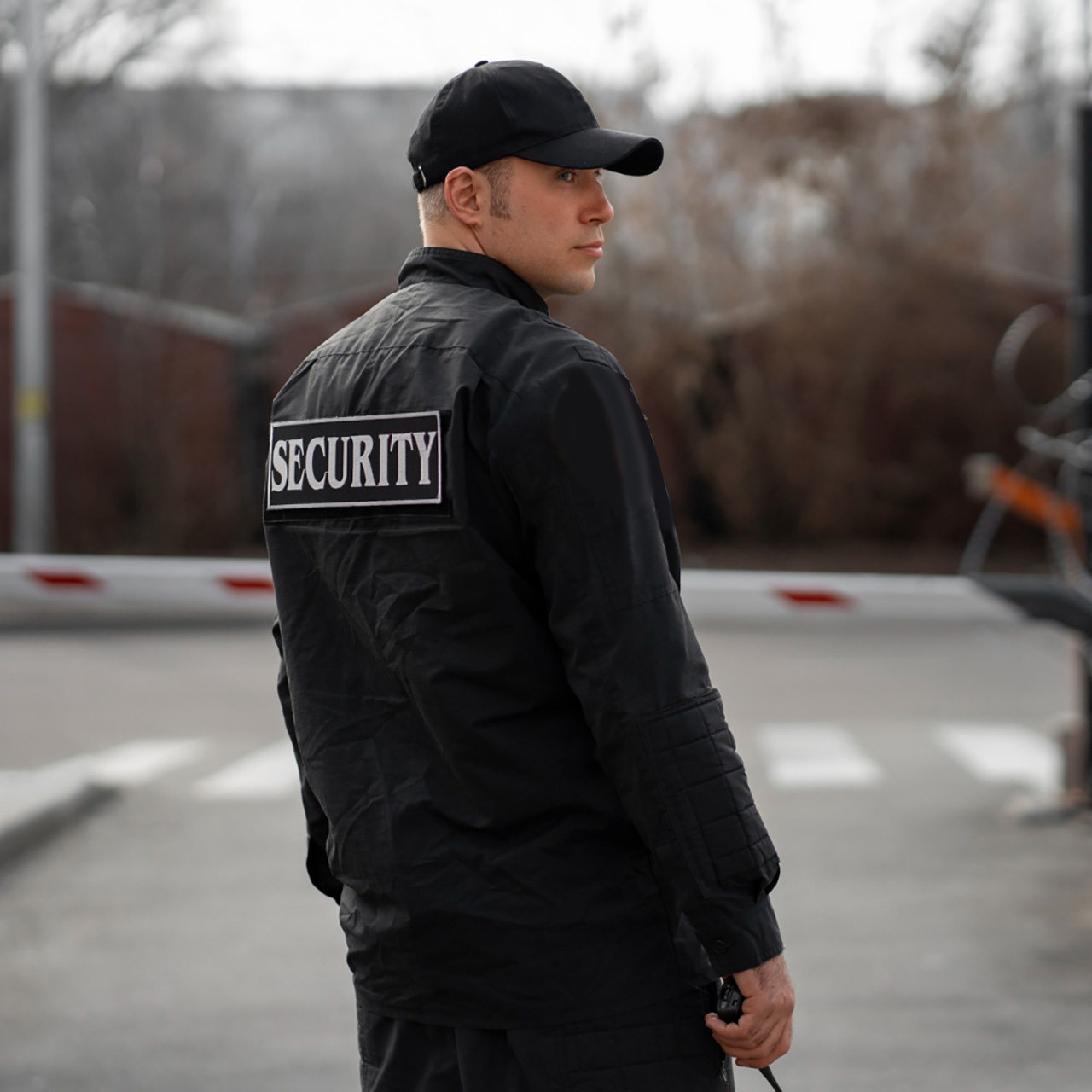 A professional security officer in a clean white uniform and cap, holding a walkie-talkie and looking alert while on duty. The uniform features a 'Security' gold embroidery and an official Guardion Protection badge.